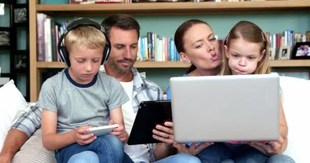 Familia usando tecnologías sentadas en el sofá — Vídeo de stock