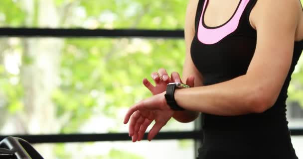 Mujer usando bicicleta estática y reloj inteligente — Vídeos de Stock