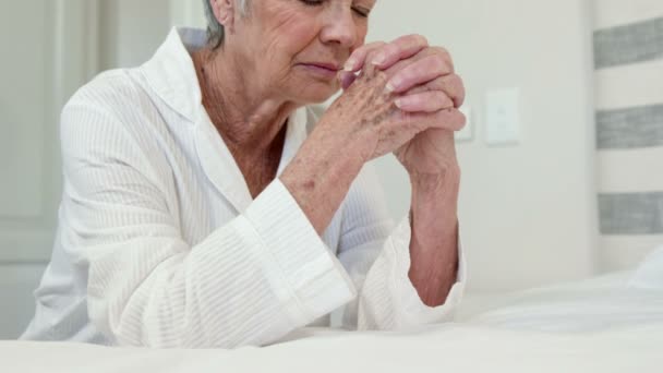 Старшая женщина молится на кровати — стоковое видео