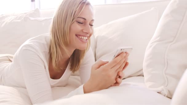 Жінка лежить на дивані, використовуючи свій смартфон — стокове відео