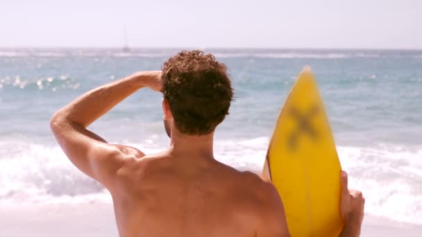 Homem está olhando para o mar com sua prancha de surf — Vídeo de Stock