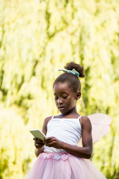 Χαριτωμένο κορίτσι μιγάδες φορώντας μια νεράιδα φόρεμα και χρησιμοποιώντας ένα smartphon — Φωτογραφία Αρχείου