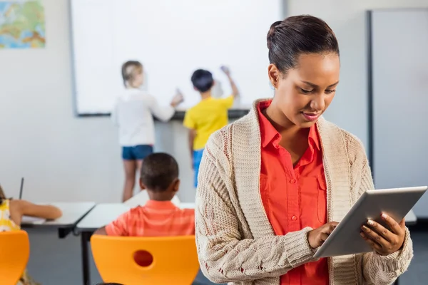 Um professor usando tablet enquanto os alunos trabalham — Fotografia de Stock