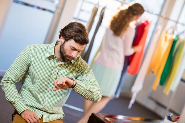 Bored man waiting his wife while woman by clothes rack — Stock Photo, Image