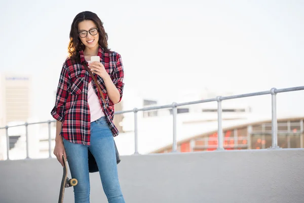 Hipster met een skateboard en smartphone — Stockfoto