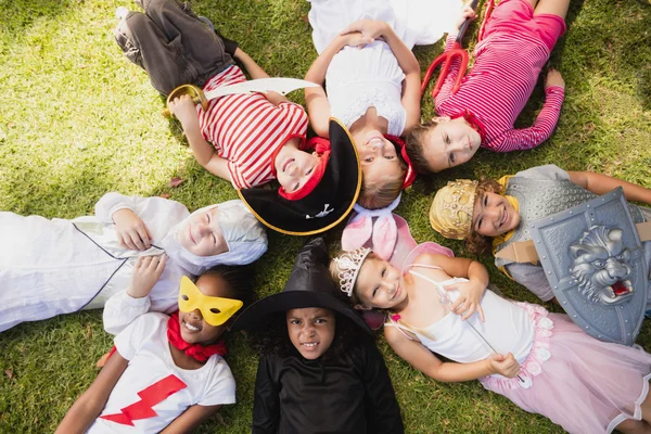 Дети в маскарадных платьях лежат на траве и смотрят в камеру — стоковое фото