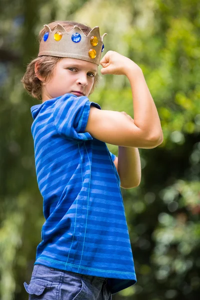 Porträt eines süßen Jungen mit einer Krone, die seine Muskeln zeigt — Stockfoto