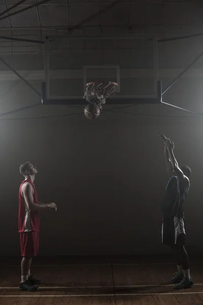 Два баскетболиста в спортзале, один забивает мяч. — стоковое фото