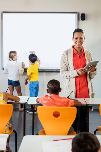 Lachende leraar poserend met tablet pc in de klas — Stockfoto