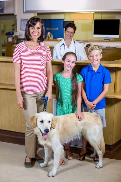 Famiglia felice in posa con il loro cane di fronte a un veterinario sorridente — Foto Stock