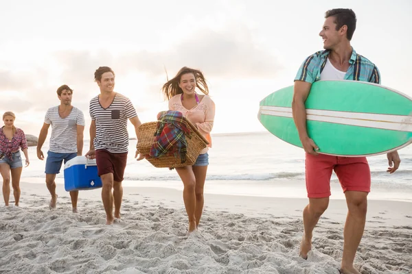 Friends carrying a surfboard and basket — Stock Photo, Image