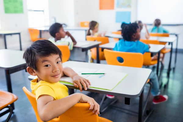 Leerling zit aan zijn bureau kijken camera in klas — Stockfoto