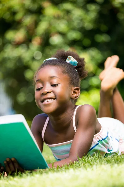 Sonriendo linda chica de raza mixta mintiendo y leyendo un libro — Foto de Stock