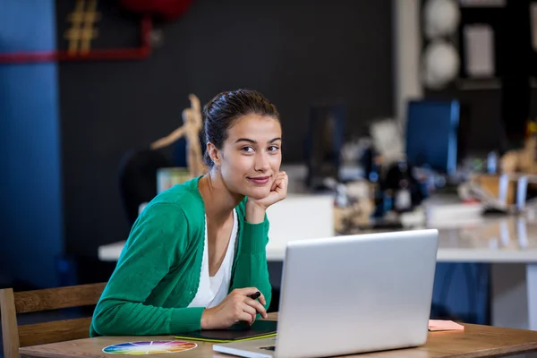 Mujer de negocios sonriendo a la cámara mientras se sienta en el escritorio —  Fotos de Stock