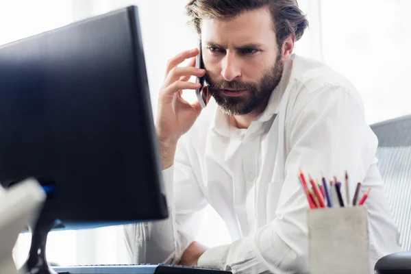 A man passing a call in front of his computer — Stock Photo, Image