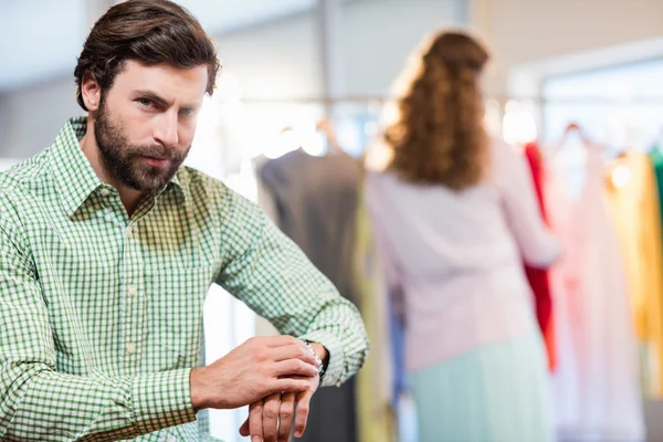 Homem entediado esperando sua esposa enquanto mulher por roupas rack — Fotografia de Stock