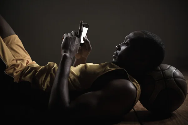 Basketballer liegen en het gebruik van zijn smartphone — Stockfoto