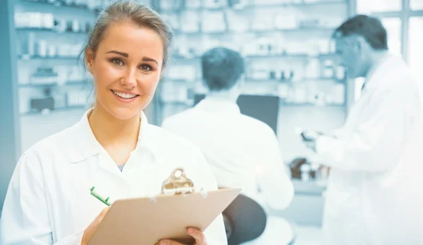 Junior pharmacist writing on clipboard — Stock Photo, Image