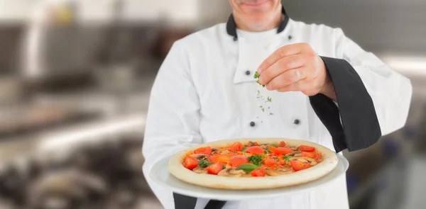 Koch hält eine Pizza in der Hand und fügt Kräuter hinzu — Stockfoto