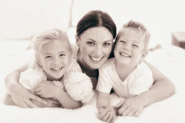 Gelukkig moeder en haar kinderen liggend op een bed — Stockfoto