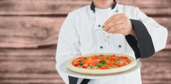 Chef segurando uma pizza e adicionando ervas — Fotografia de Stock