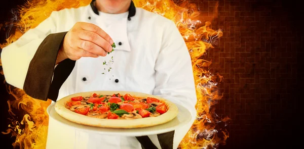 Koch hält eine Pizza in der Hand und fügt Kräuter hinzu — Stockfoto