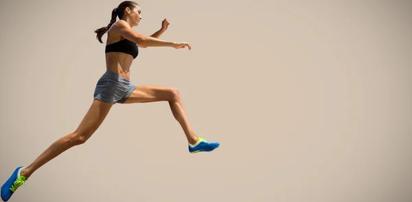 Sportskvinne som hopper mot beige bakgrunner – stockfoto