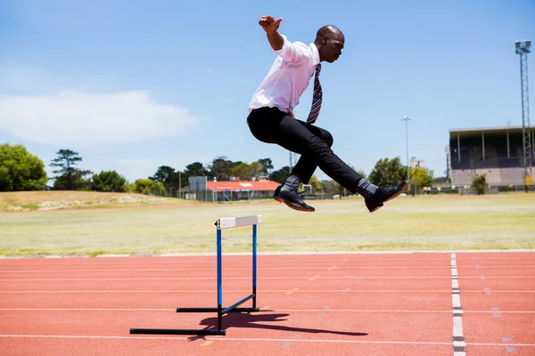 Businessman jumping hurdle while running — Stock Photo, Image