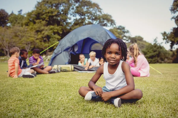 Leende kid poserar på gräs under en solig dag med andra barn — Stockfoto