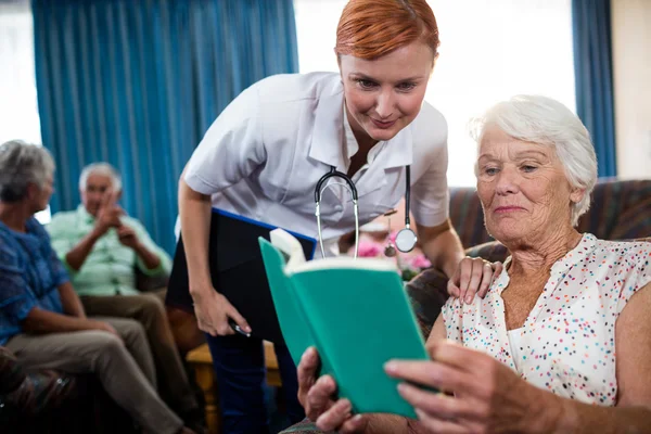 Äldre kvinna läser bok med sjuksköterska — Stockfoto
