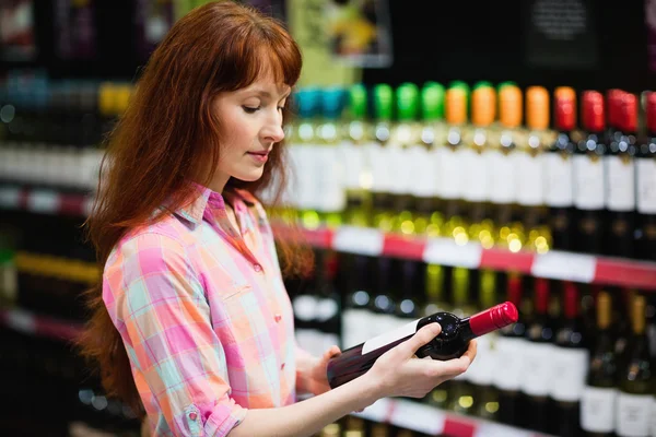 Woman choosing carefully bottle of wine — Stock Photo, Image