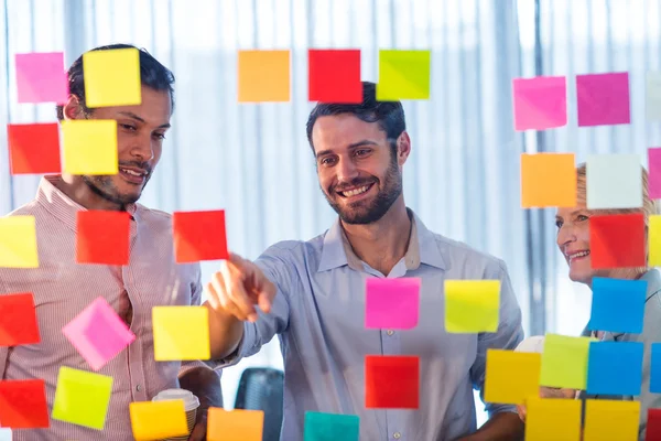 Business people looking at post it on wall — Stock Photo, Image