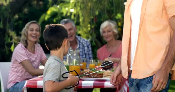 Famiglia alla ricerca di un ragazzo che prepara il barbecue — Video Stock