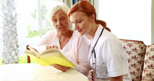 Sjuksköterska och gammal kvinna läsa bok — Stockvideo