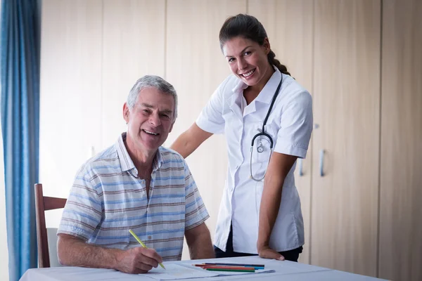 Médecin et senior souriant tout en dessinant — Photo