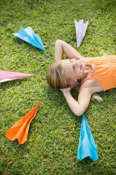 Jong meisje liggen op gras rond papier vliegtuigen — Stockfoto