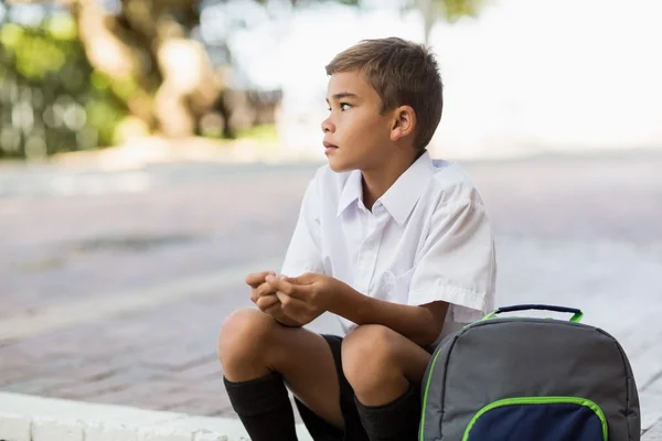 Thoughtful schoolboy sitting in campus — Stock Photo, Image