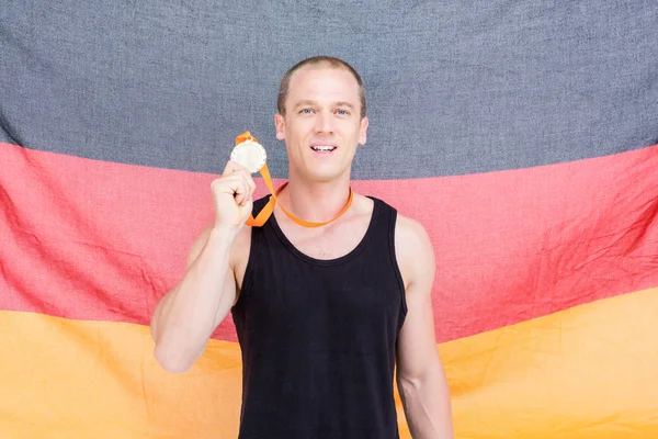 Atleta mostrando sua medalha de ouro na frente da bandeira alemã — Fotografia de Stock