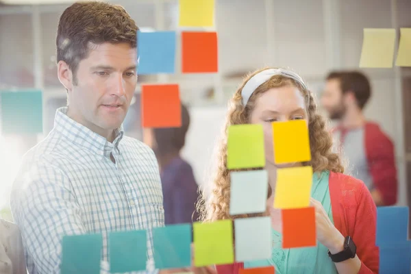 Business people looking at post it on wall — Stock Photo, Image