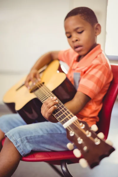 Schoolboy playing guitar in classroom — Stock Photo, Image