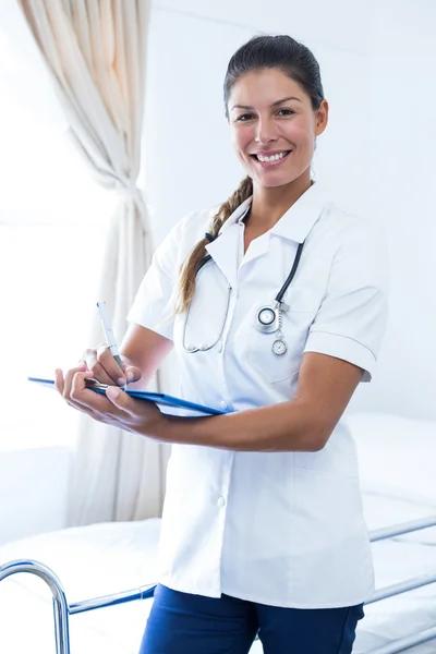 Portrait of female doctor writing on clipboard in hospital — Stock Photo, Image