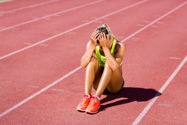 Upset female athlete sitting on running track clipart