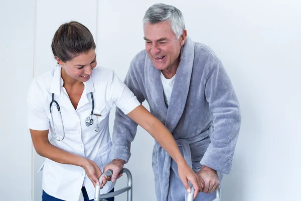 Female doctor helping senior man to walk with walker — Stock Photo, Image