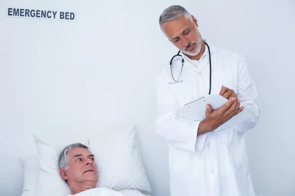 Male doctor writing medical report of senior man on clipboard — Stock Photo, Image