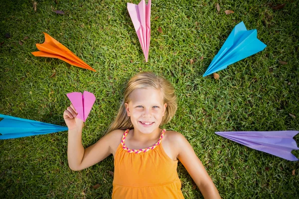 Chica joven acostada en la hierba alrededor de aviones de papel — Foto de Stock