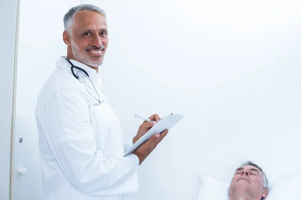 Male doctor writing medical report of senior man on clipboard — Stock Photo, Image