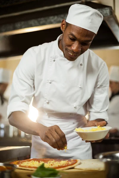 Chef polvilhando queijo em uma pizza — Fotografia de Stock