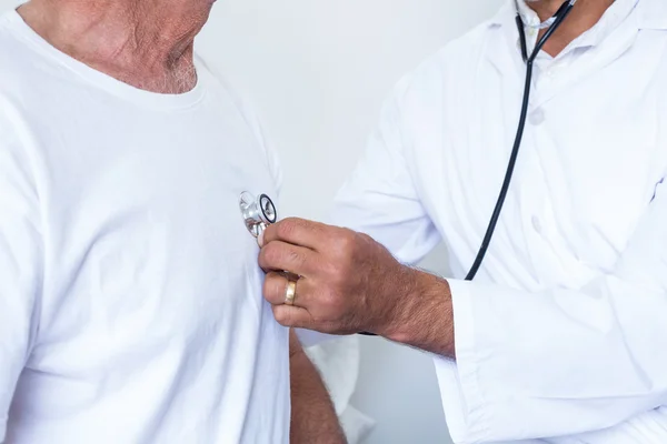 Male doctor checking heartbeat of senior man — Stock Photo, Image