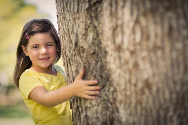 Χαμογελώντας αγκαλιάζει κορμό δέντρου κορίτσι στο πάρκο — Φωτογραφία Αρχείου