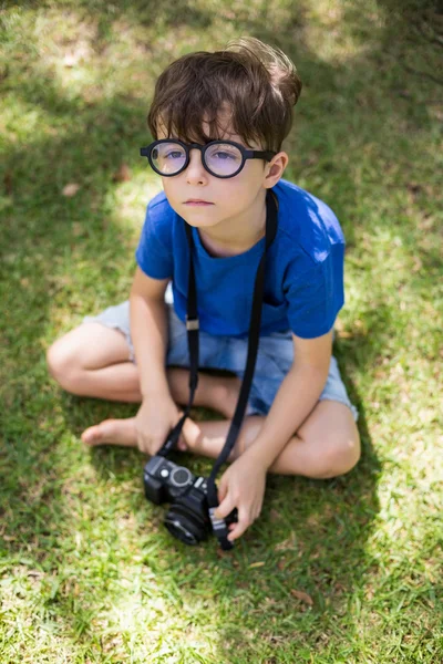 Pojken sitter på gräset med en kamera — Stockfoto